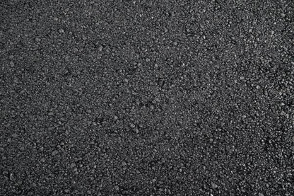 A close-up view of black asphalt, showing a rough, textured surface. The Cold-Lay Patching Tarmac by Brisks appears to be newly laid, with small stones and gravel compacted together, creating a coarse and granular appearance.