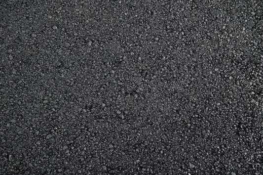A close-up view of black asphalt, showing a rough, textured surface. The Cold-Lay Patching Tarmac by Brisks appears to be newly laid, with small stones and gravel compacted together, creating a coarse and granular appearance.