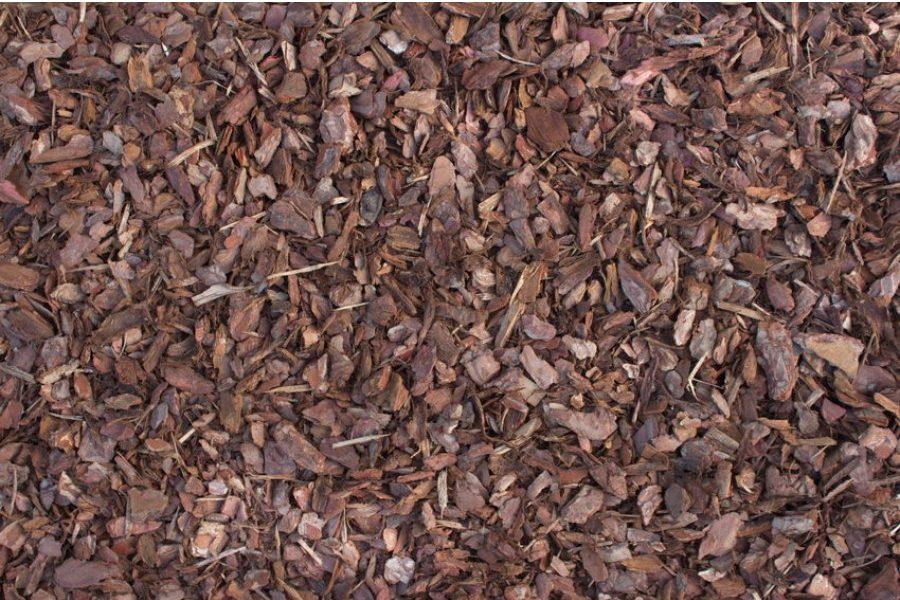 A close-up view of a ground covered in Brisks Playground Bark. The small, irregularly shaped pieces of wood are varying shades of brown, creating a textured, earthy surface commonly used in landscaping and gardening.