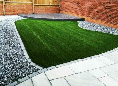 A tidy backyard with a neatly mowed green lawn in a curved shape, surrounded by gray gravel and Brisks 20mm Polar Black Ice Chippings along a light stone walkway. A wooden deck is positioned towards the back, adjacent to a tall brick wall and wooden fence.