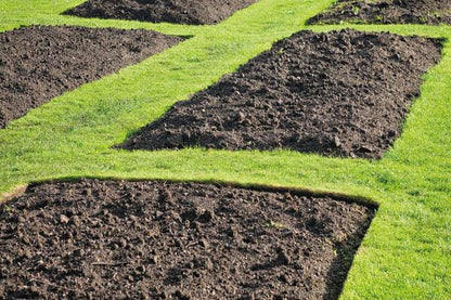 Rectangular plots of tilled soil arranged in rows with well-manicured grass pathways in between each plot. The dark, premium quality Brisks Multipurpose Garden Topsoil appears ready for planting, enriched with essential soil nutrients. The green grass contrasts beautifully with the rich brown earth.