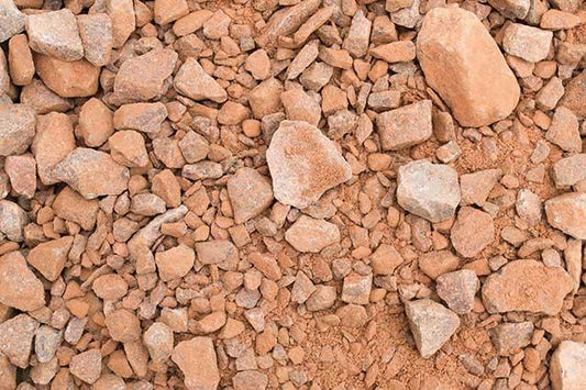 A close-up view of a pile of Brisks MOT Type 1 Frost Resistant, comprising various sizes from small pebbles to medium-sized stones. The texture is rough with jagged edges. The overall color is a mix of reddish and earthy tones, ideal for sub-base applications.